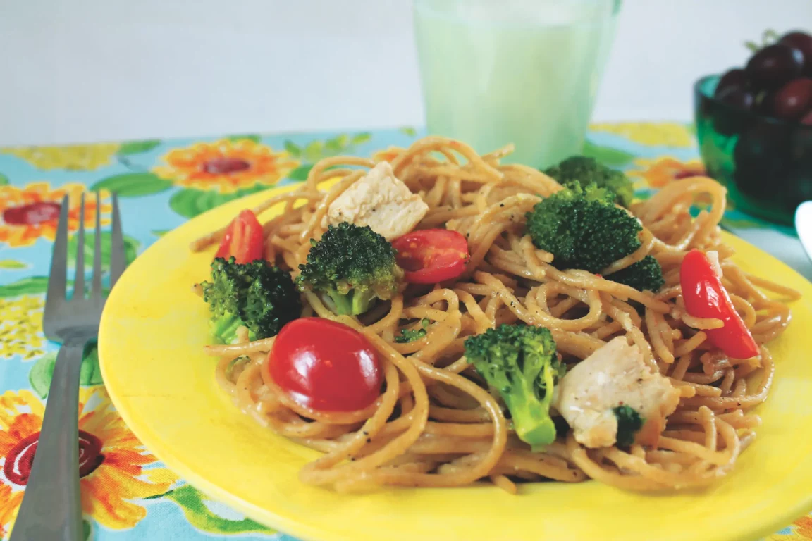 Spaghetti is plated with broccoli, tomato, and mushrooms