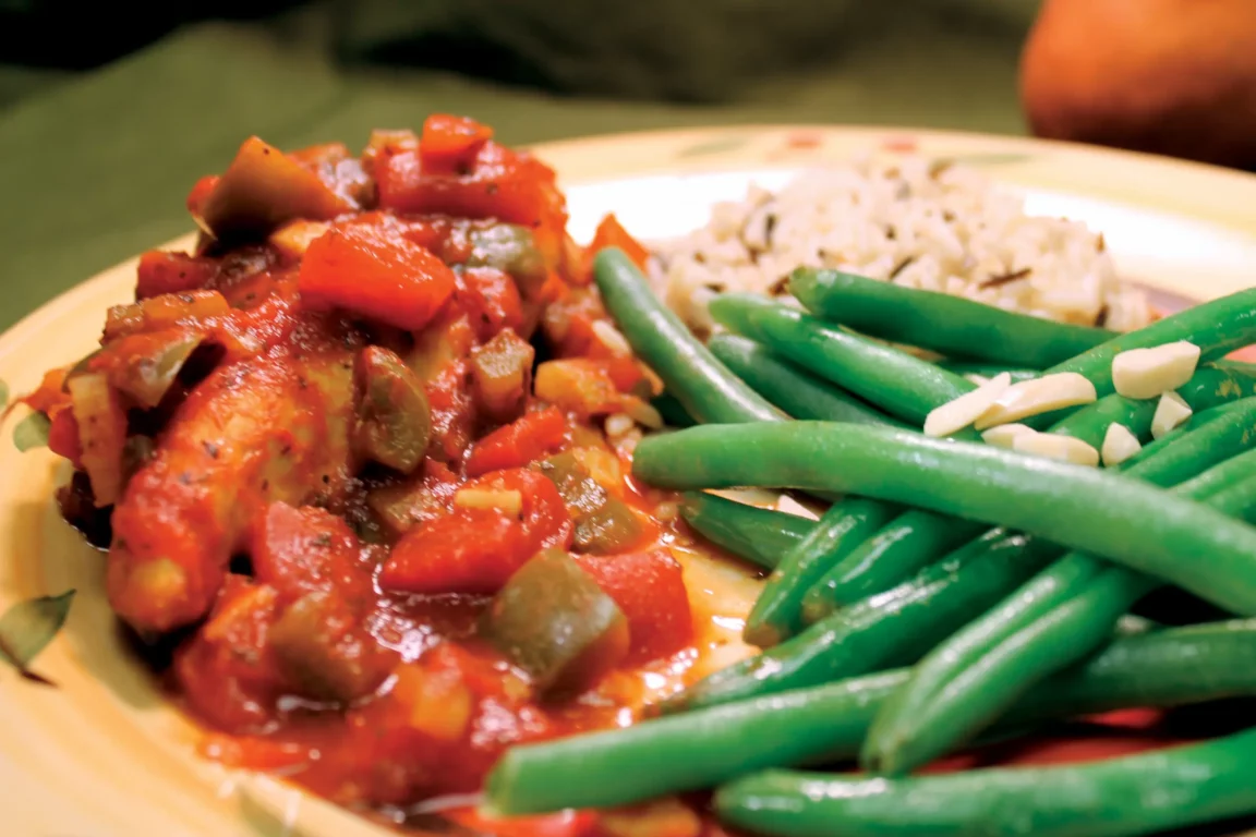 Chicken Creole is plated with brown rice and green beans.