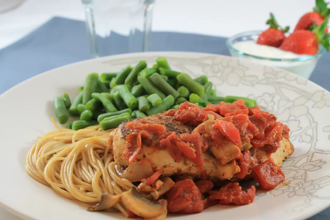 Chicken Cacciatore plated on top of spaghetti, paired with green beans. 