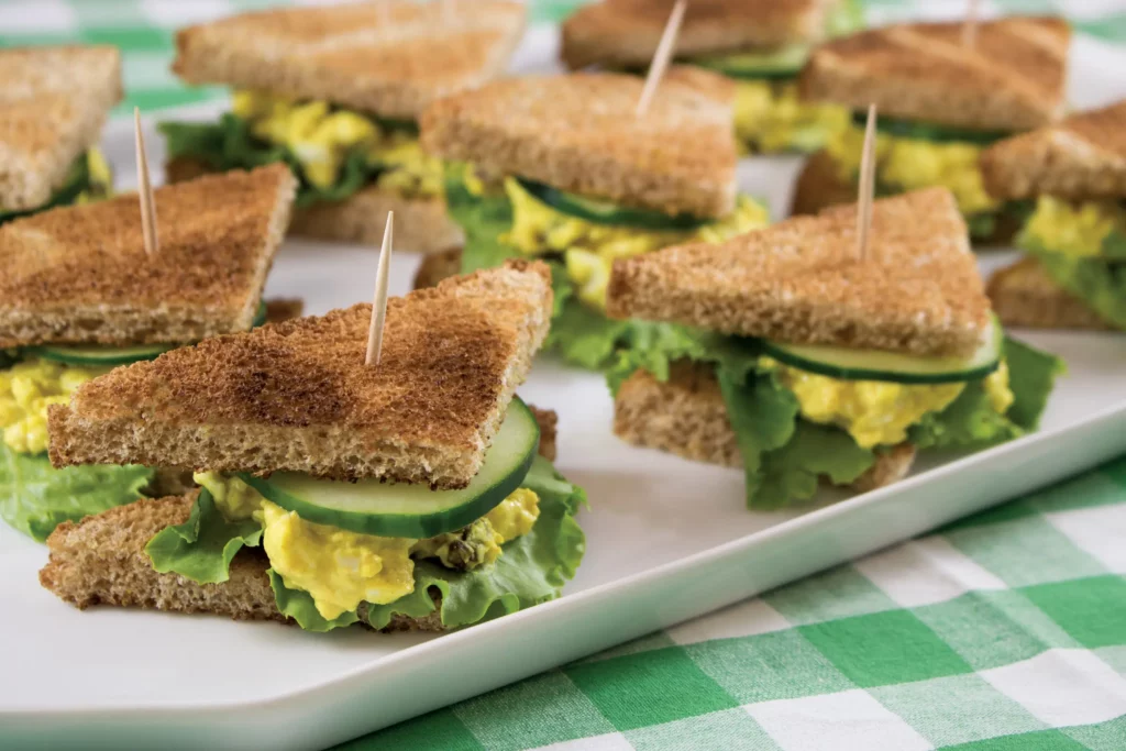 triangle cut sandwiches of curried egg salad topped with cucumber