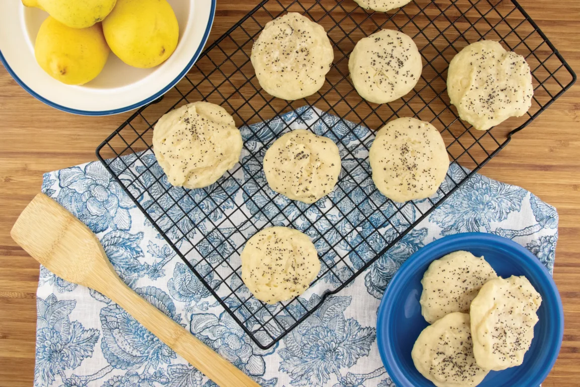 Lemon Ricotta cookies topped with poppy seeds placed on a cooking rack on top of a blue napkin