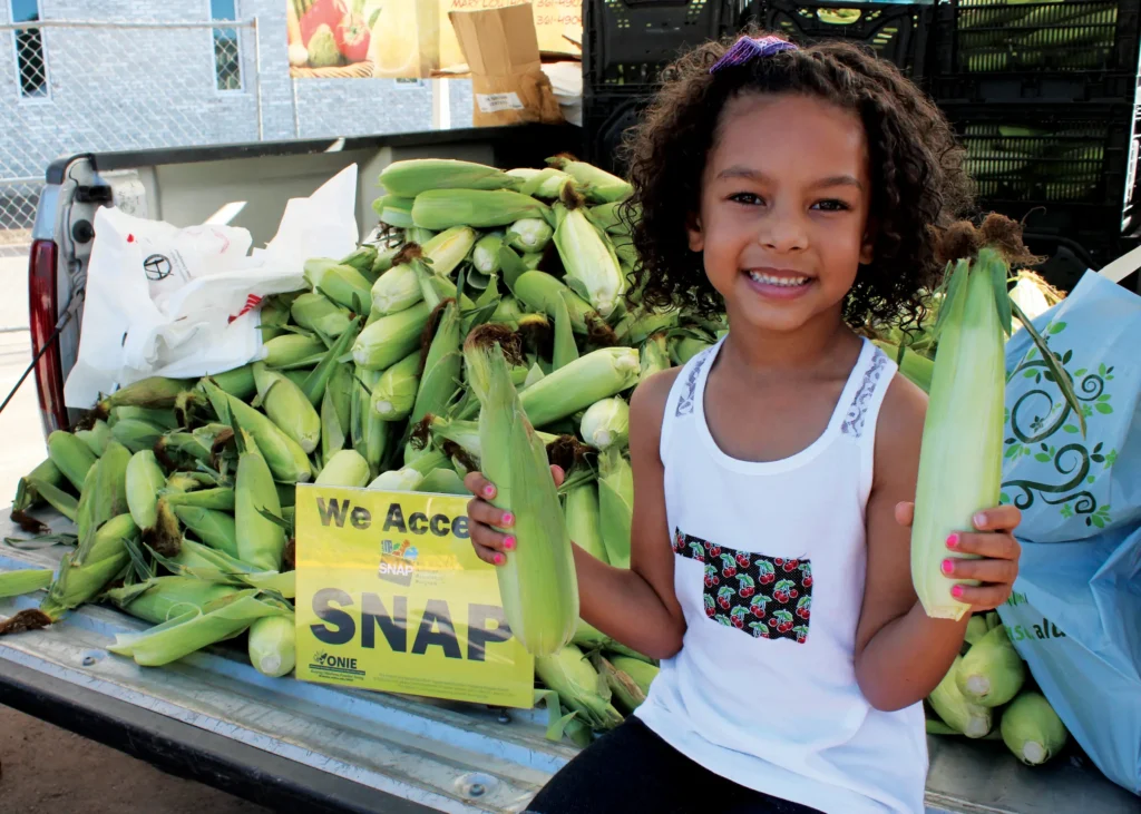 girl holding corn at farmers market.